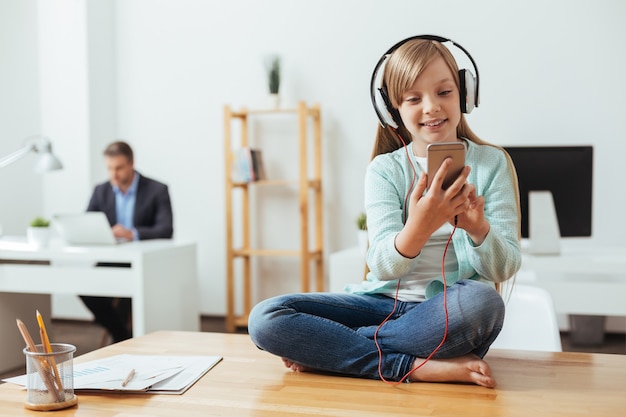 Savvy smart girl gaie à l'aide de son téléphone pour choisir la bonne chanson tout en portant des écouteurs