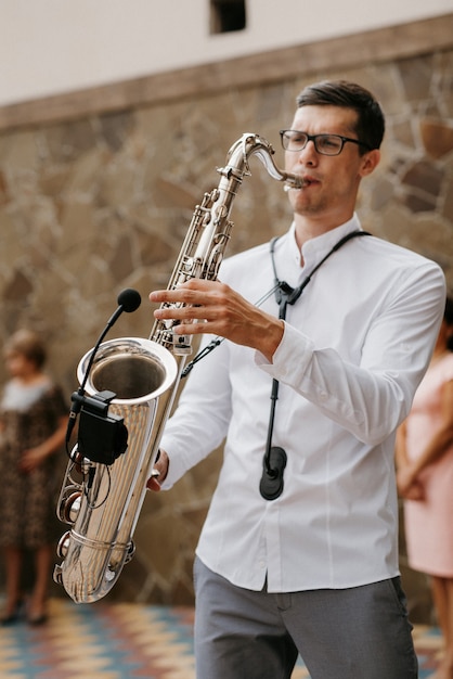 Le saxophoniste musicien en chemise blanche joue du saxophone chromé