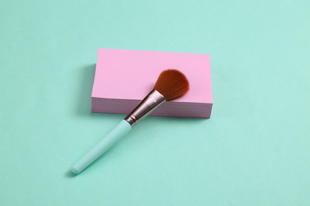 Scène de beauté minimaliste Pinceau de maquillage avec plate-forme rose sur fond bleu