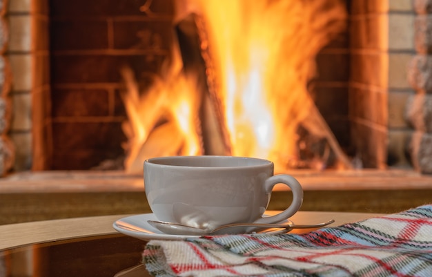 Scène de cheminée confortable, le thé se verse dans une tasse blanche, des biscuits sur une table.