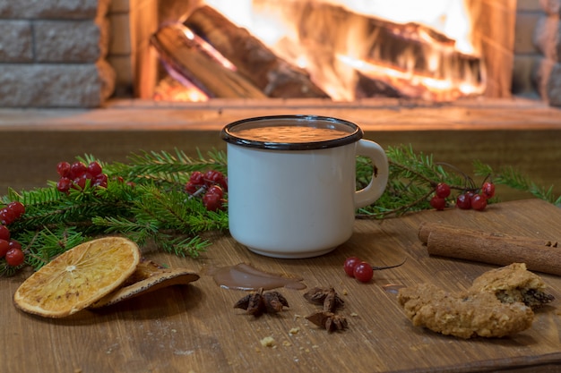 Scène confortable devant la cheminée avec une tasse blanche émaillée de chocolat chaud, d&#39;épices et de fruits confits.