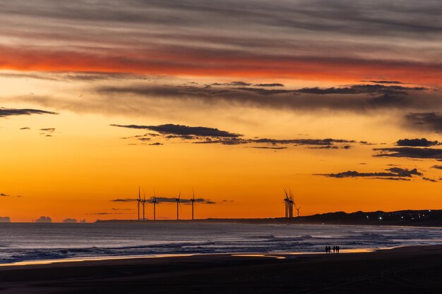 Scène d'un coucher de soleil sur la mer avec des silhouettes de moulins à vent et de gens