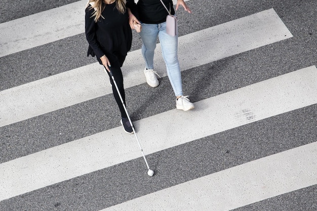 Scène d'une femme aveugle marchant sur un passage clouté aidée par une autre personne utilisant sa canne blanche