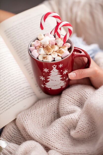 Scène magique de Noël, ambiance feutrée. Femme tenant une tasse de boisson avec des guimauves.