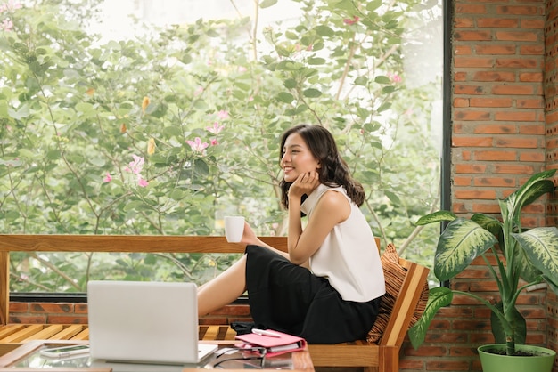 Scène matinale de la main droite de la jeune femme écrivant sur un ordinateur portable à côté de la fenêtre du café. Mode de vie de travail indépendant