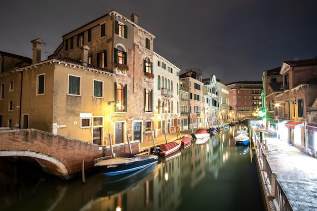 Scène nocturne de vieux bâtiments illuminés, de bateaux flottants et de reflets dans l'eau du canal à Venise, en Italie.