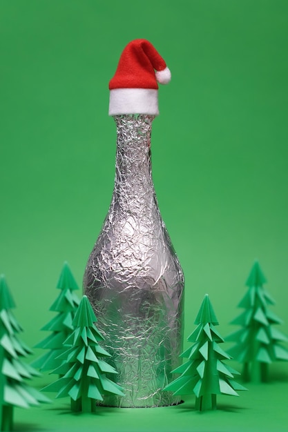 Scène de Noël festive avec bouteille de champagne et sapin vert en origami. Carte de nouvel an et de Noël sur fond vert. Fond de nouvel an avec sapin en papier. Bouteille de champagne avec Bonnet de Noel