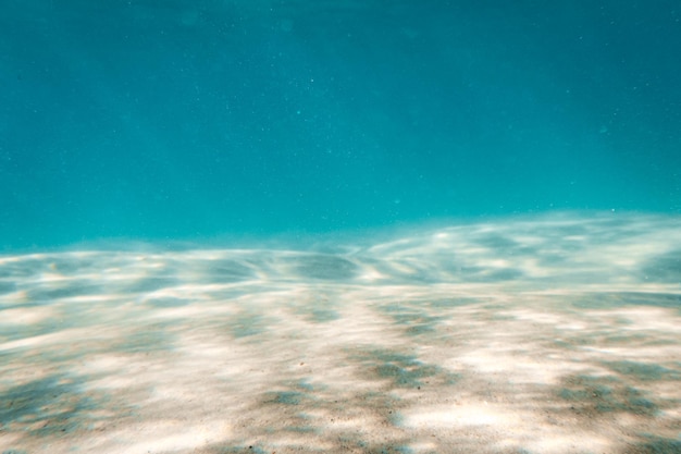Scène sous-marine avec des rayons de soleil traversant l'eau et reflétés sur fond de sol de sable
