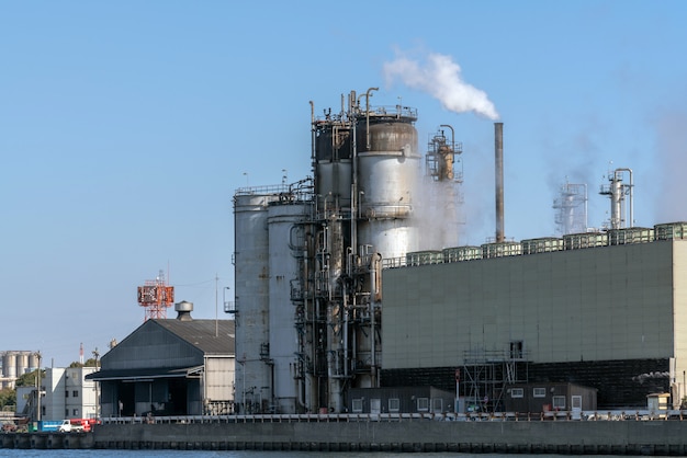 Scène de la zone industrielle de la raffinerie de pétrole au bord de la rivière à l’heure de travail, fumée fumée