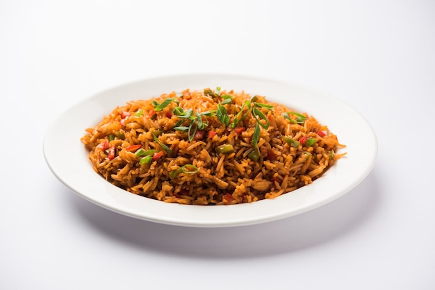 Schezwan Fried Rice Masala est un aliment indo-chinois populaire servi dans une assiette ou un bol avec des baguettes