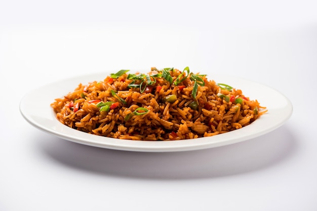 Schezwan Fried Rice Masala est un aliment indo-chinois populaire servi dans une assiette ou un bol avec des baguettes