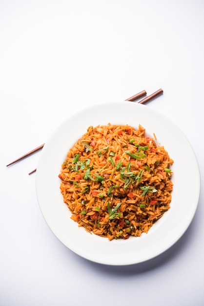 Schezwan Fried Rice Masala est un aliment indo-chinois populaire servi dans une assiette ou un bol avec des baguettes