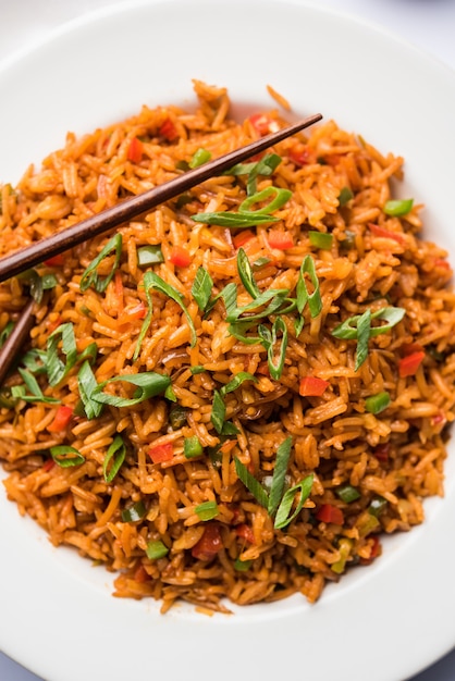 Schezwan Fried Rice Masala est un aliment indochinois populaire servi dans une assiette ou un bol avec des baguettes. mise au point sélective