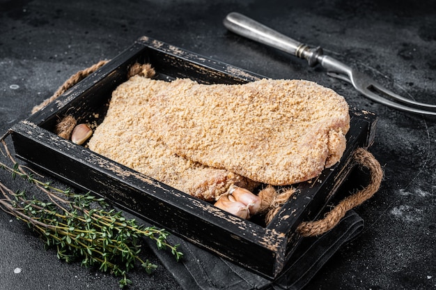 Schnitzel cru allemand fait maison dans un plateau en bois. Fond noir. Vue de dessus.