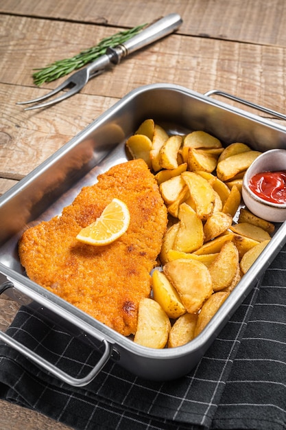 Schnitzel weiner de viande de porc avec quartiers de pommes de terre et sauce tomate dans un plateau en acier Fond en bois Vue de dessus