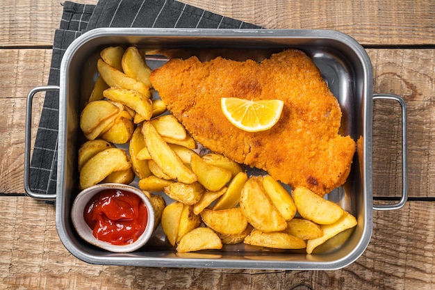 Schnitzel weiner de viande de porc avec quartiers de pommes de terre et sauce tomate dans un plateau en acier Fond en bois Vue de dessus