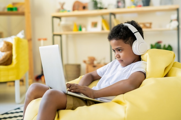 Schoolkid adorable concentré dans des écouteurs regardant l'écran de l'ordinateur portable tout en jouant à un jeu ou en suivant un cours éducatif en ligne