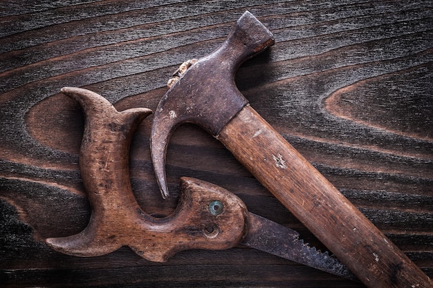 Scie à main rétrostyle en métal rouillé et marteau à griffes avec poignées en bois sur le concept de construction de fond en bois foncé vintage