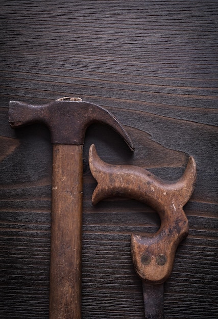 Scie à main rouillée et marteau à griffes sur fond de bois vintage