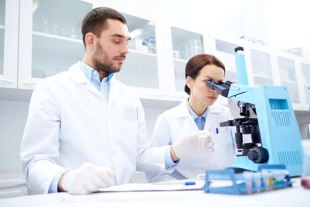 science, chimie, technologie, biologie et concept humain - jeunes scientifiques avec microscope faisant des tests ou des recherches en laboratoire clinique et prenant des notes