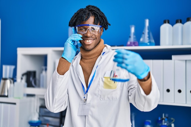 Photo scientifique afro-américain parlant sur le smartphone tenant un tube à essai au laboratoire