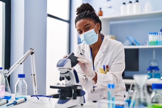 Scientifique afro-américaine portant un masque médical à l'aide d'un microscope au laboratoire