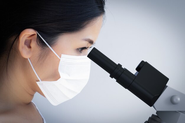 Scientifique asiatique portant un masque facial et regardant un microscope