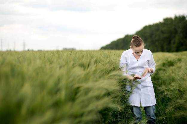 Scientifique en blouse blanche regardant les plantes vertes sur le terrain