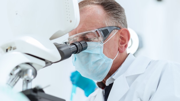 scientifique dans un masque de protection regardant à travers un microscope.