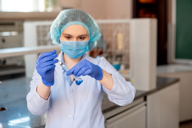 Scientifique faisant des recherches en laboratoire. Professionnel de la science féminine focalisée tenant une solution bleue dans la cuvette en verre