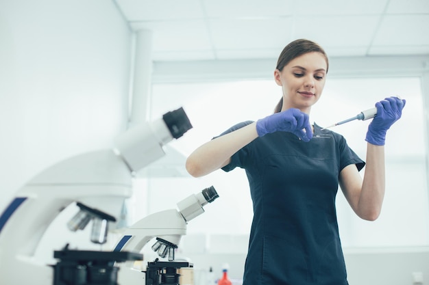 Scientifique de laboratoire professionnel souriant et laissant tomber un échantillon sur une lame de microscope