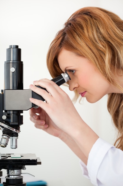 Scientifique mignon aux cheveux blonds regardant à travers un microscope