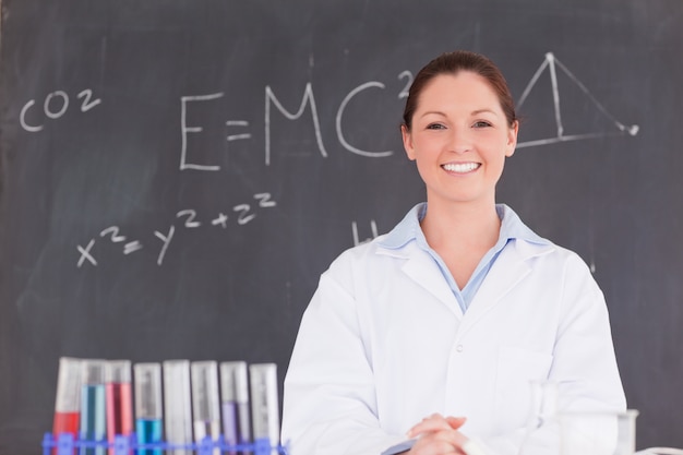 Scientifique mignon debout devant un tableau en regardant la caméra