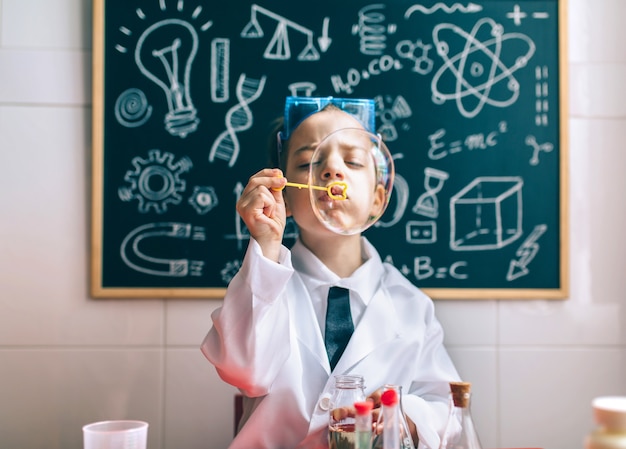 Scientifique de petit garçon jouant avec des bulles de savon contre le tableau noir dessiné