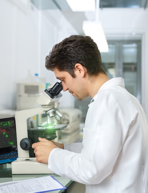 Un scientifique ou un technicien aux cheveux noirs et aux yeux bruns travaille avec des échantillons de microscope