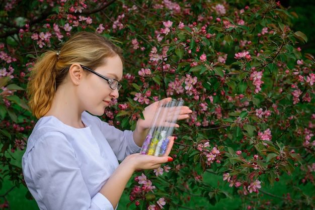 Une scientifique avec des tubes à essai étudie les propriétés des plantes dans le jardin botanique, les parfums floraux, les cosmétiques naturels, la phytothérapie et les parfums