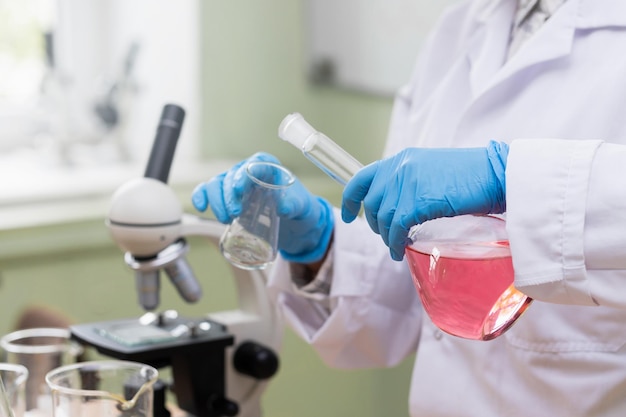 Scientifique versant une substance rose d'un flacon à l'autre dans un laboratoire pendant les travaux de recherche