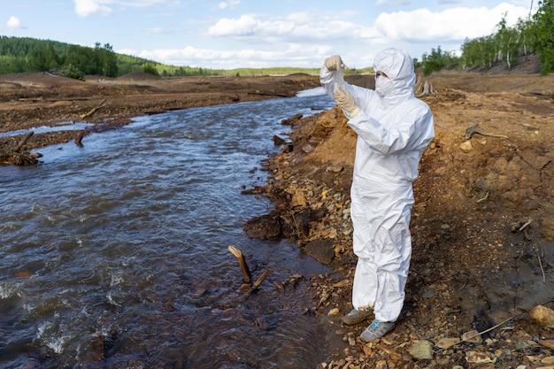 Un scientifique vêtu d'une combinaison de protection blanche prend des échantillons d'eau d'une rivière polluée.