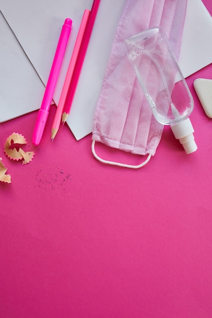 Scolarité à plat après la pandémie de coronavirus, Retour à l'école dans une nouvelle réalité, Fournitures scolaires, masque de protection et antiseptique sur fond rose, espace pour le texte