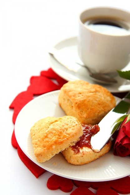 Scones en forme de coeur avec de la confiture de fraises et une tasse de thé