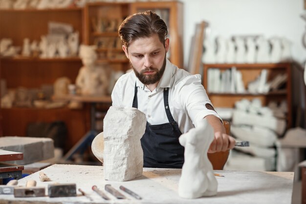 Le sculpteur barbu mesure le torse d'une femme en pierre pour en faire une copie à partir de calcaire au studio de création.