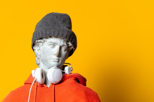 Sculpture d'adolescent en sweat à capuche orange et casque sur fond jaune