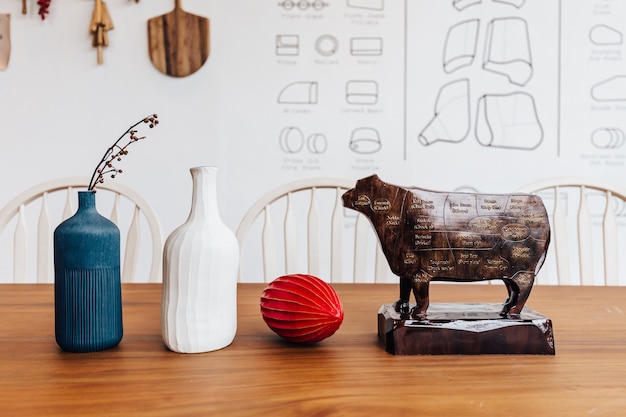 Photo sculpture en bois de vache avec une coupe de viande de bœuf de diagramme sur elle avec un pot bleu et blanc et des fruits rouges sur une table en bois.