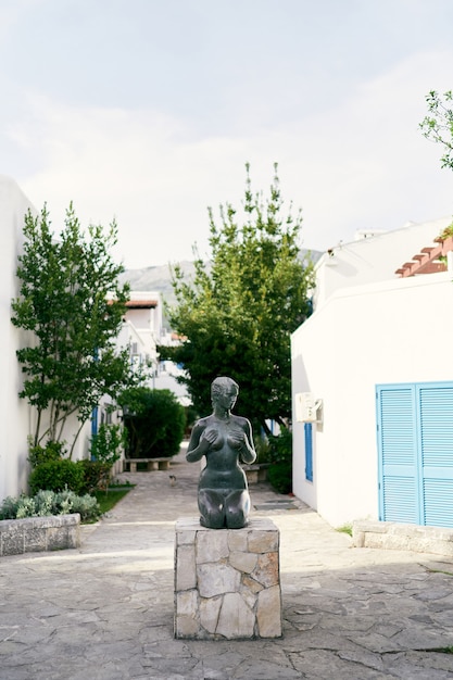 Sculpture d'une fille nue assise sur un piédestal devant des bâtiments