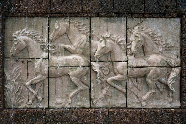 Sculpture sur pierre de chevaux sur le mur avec chute d&#39;eau