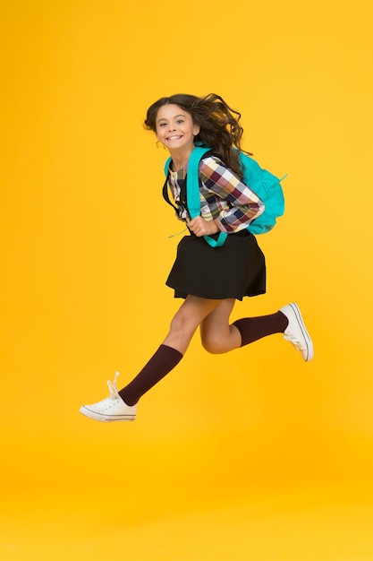 Se déplacer avec hâte Enfant énergique dans les airs fond jaune Écolière en saut énergique Retour à la mode scolaire Éléments essentiels de l'école Humeur énergique Saine et énergique