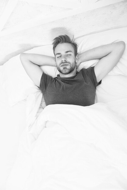 Se détendre avant de s'endormir Dormir suffisamment chaque nuit Visage d'homme barbu relaxant Maintenir un rythme circadien constant essentiel pour la santé générale Homme beau mec se détendre au lit