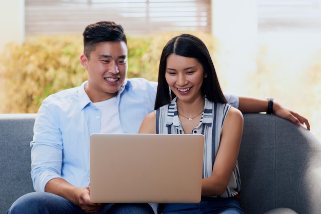 Se détendre dans la nouvelle ère Photo d'un jeune couple heureux utilisant un ordinateur portable ensemble sur le canapé à la maison