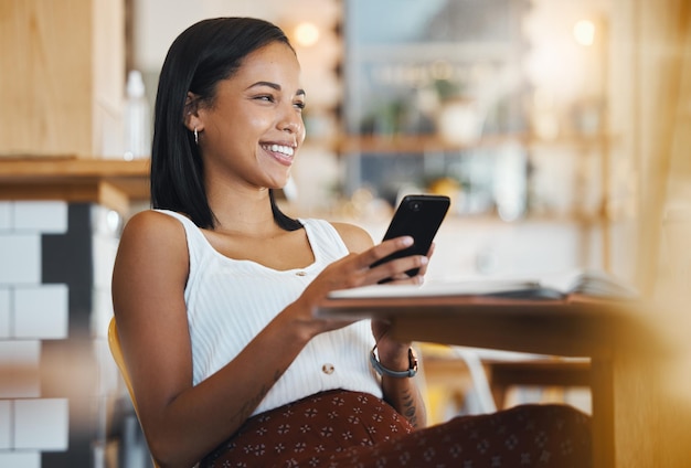 Se détendre en envoyant un message texte ou en naviguant sur les réseaux sociaux sur un téléphone par une jeune étudiante souriante dans un café Une femme heureuse pensant et recherchant sur Internet ou discutant en ligne dans un café