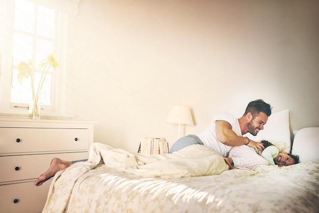 Se faire attaquer par des chatouilles Photo d'un père et d'une fille joyeux qui se battent contre des chatouilles sur le lit à la maison